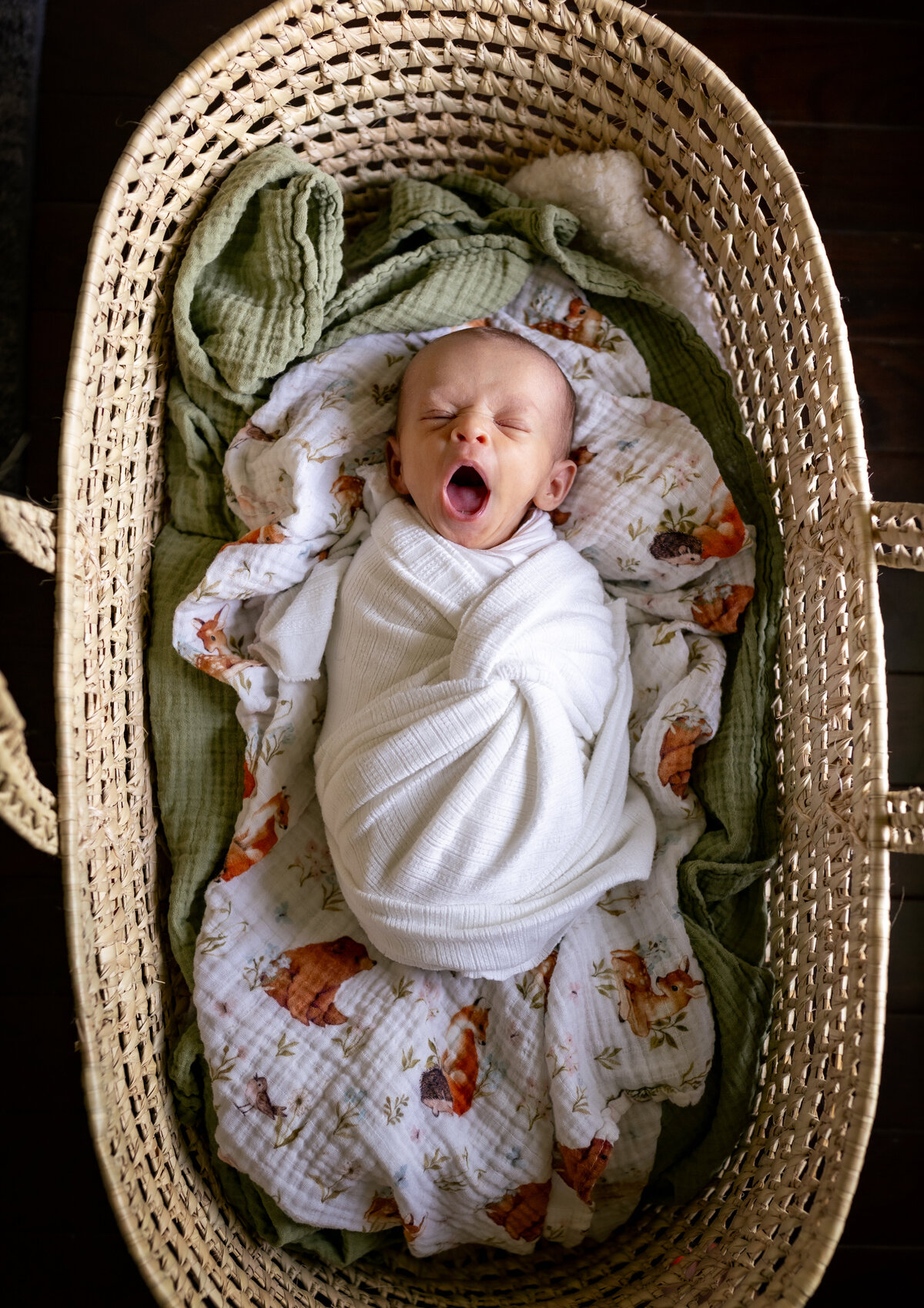 baby yawning while swaddled in wrap and lying in a bassinet