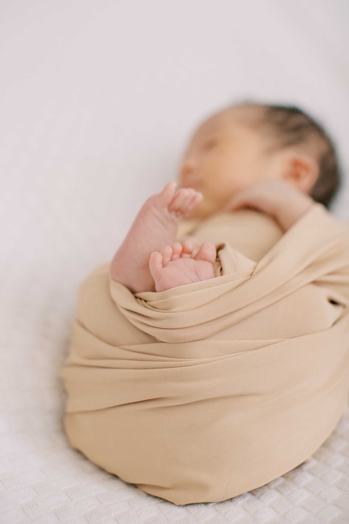 newborn baby boy wrapped in a neutral-colored swaddle with his tiny toes sticking out