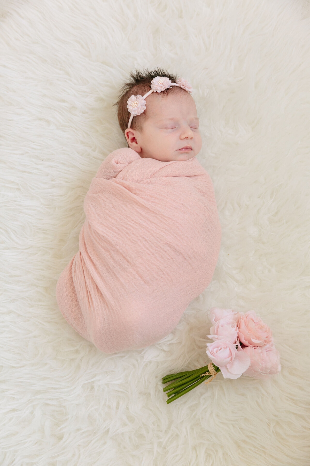 A newborn swaddled in a pink blanket with a flower next to them