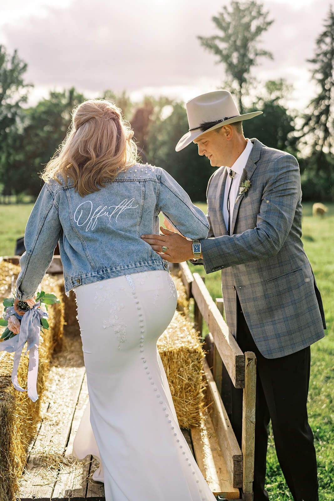 A groom helps the bride onto a hayride at their outdoor farm wedding.