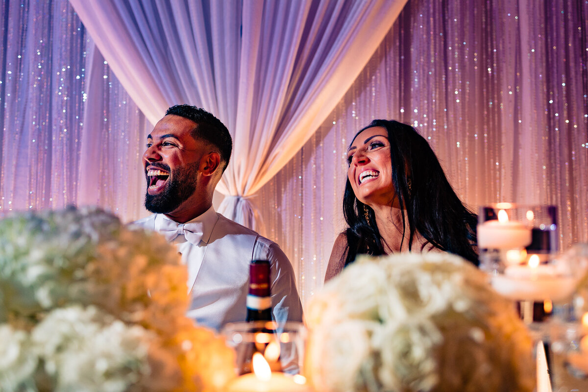 One of the top wedding photos of 2021. Taken by Adore Wedding Photography- Toledo, Ohio Wedding Photographers. This photo is of a bride and groom laughing during the speeches at their wedding reception