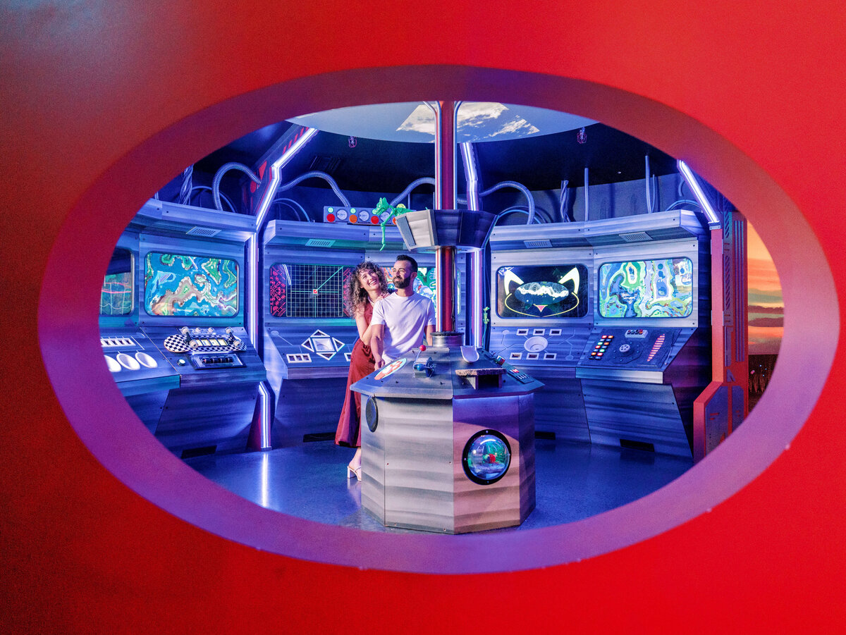 Couple posing in a vibrant, futuristic room with glowing controls at FloridaRAMA