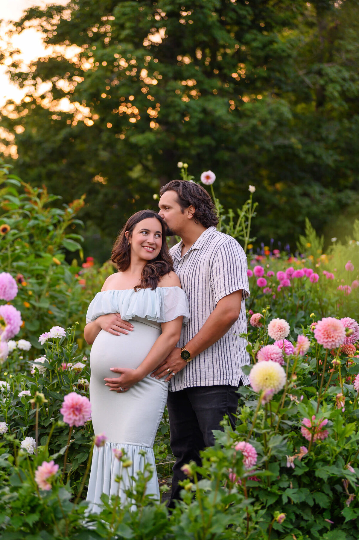 husband and wife holding mom's pregnant belly in a field of flowers for her outdoor maternity photography session in Burlington, ON