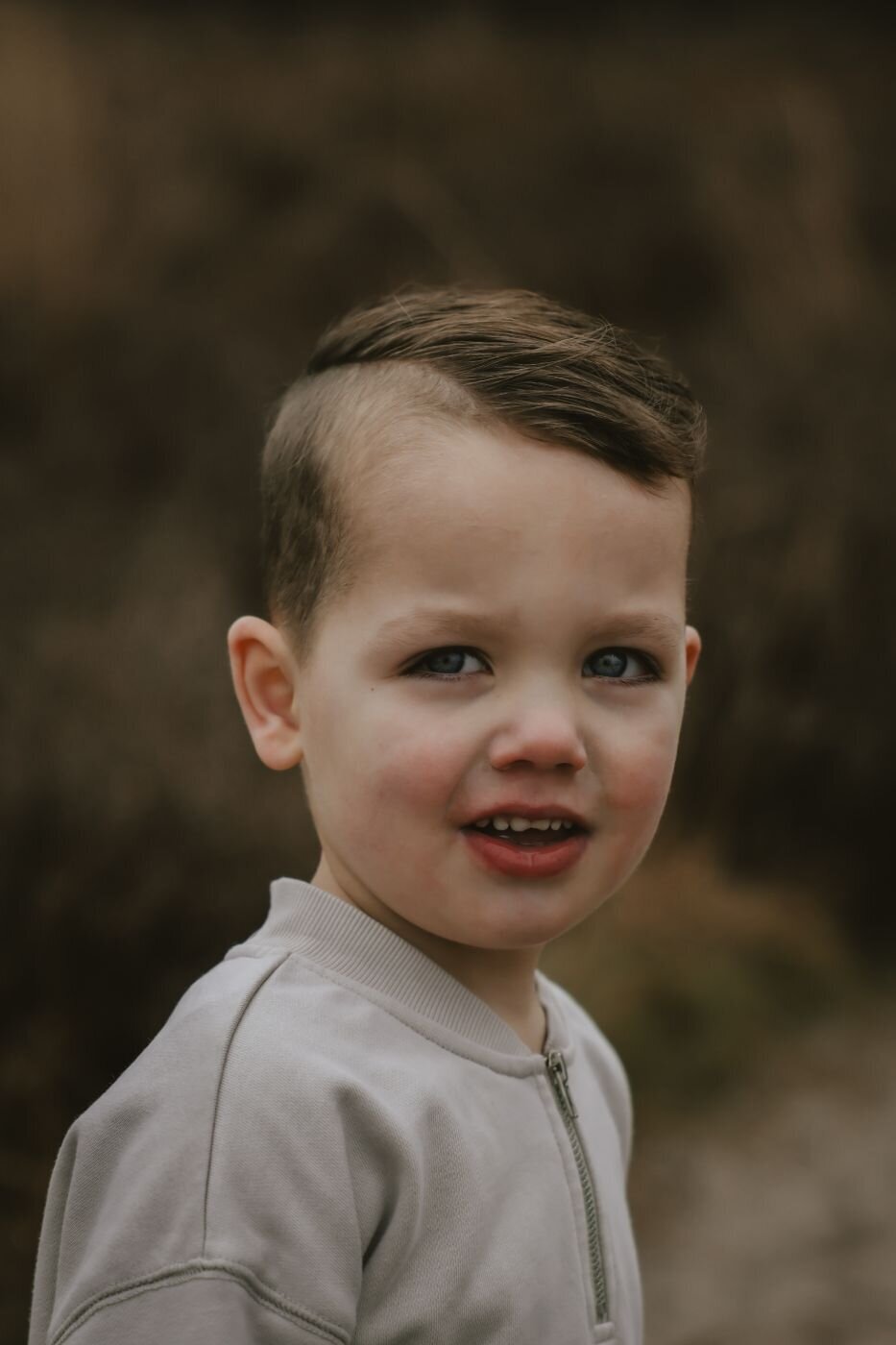 Kinderfoto. Portret van een jonge jongen met kort kapsel en een lichtgrijze sweater. Schattige jongen close-up.