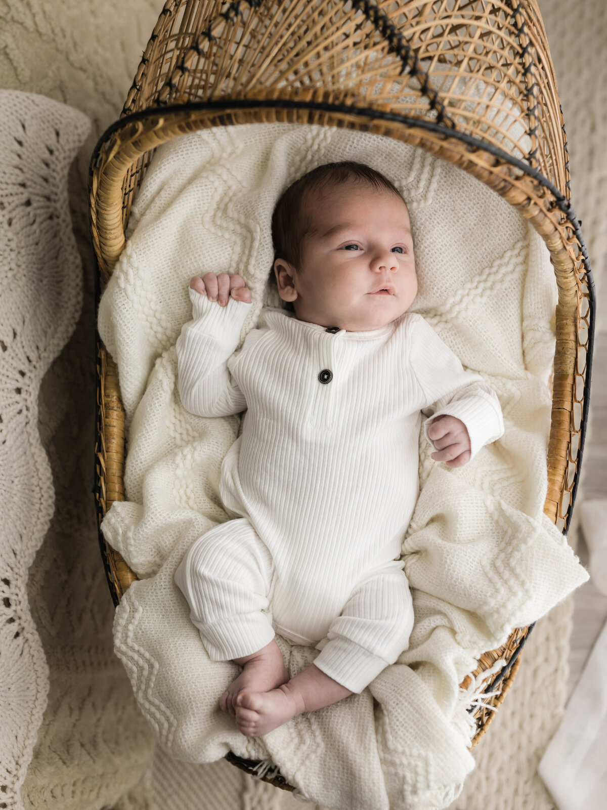 newborn baby boy in white onesie laying in bassinet for studio lifestyle session 