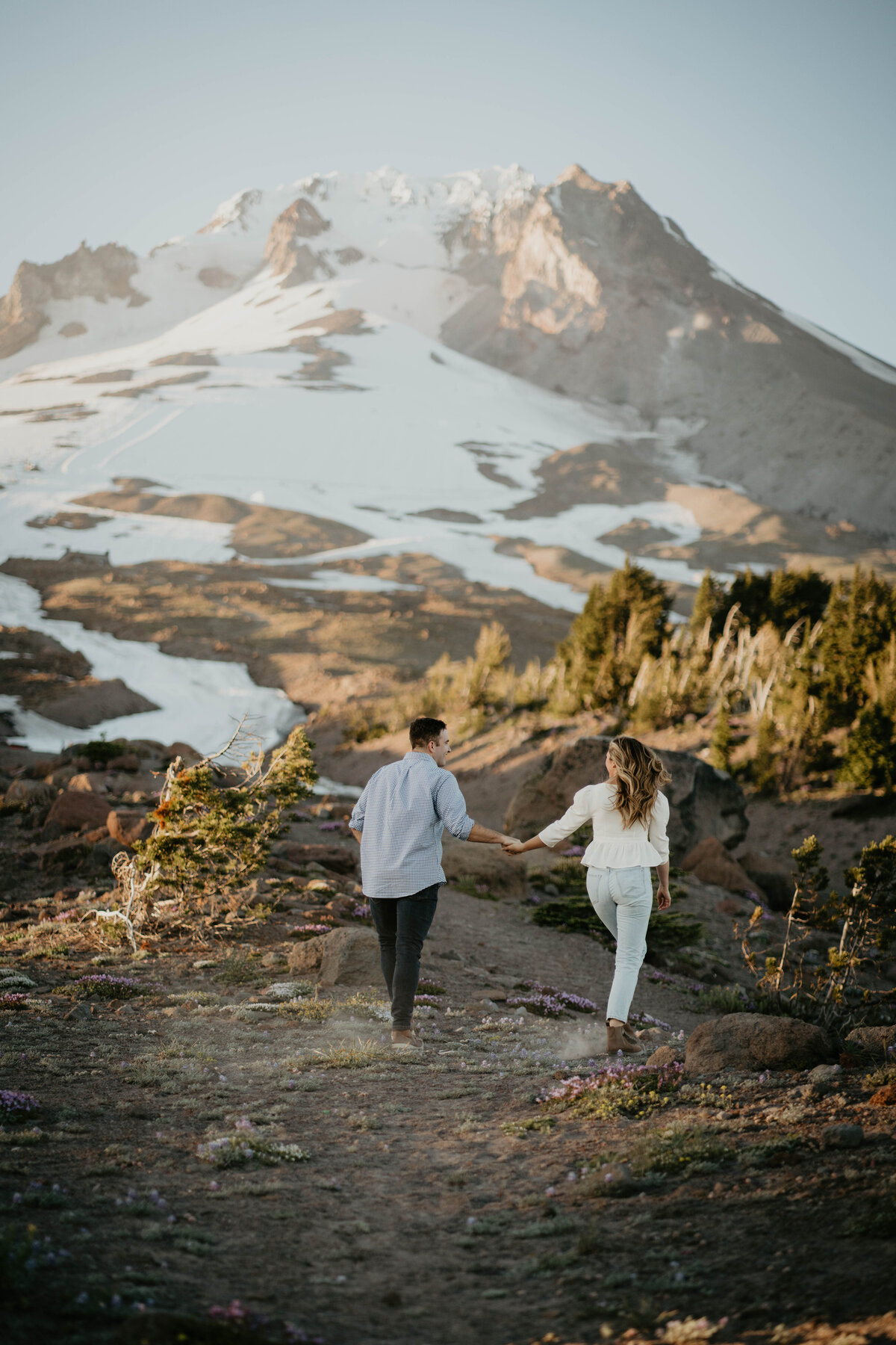 Couple holding hands and hiking with views of Mt Hood during engagement session