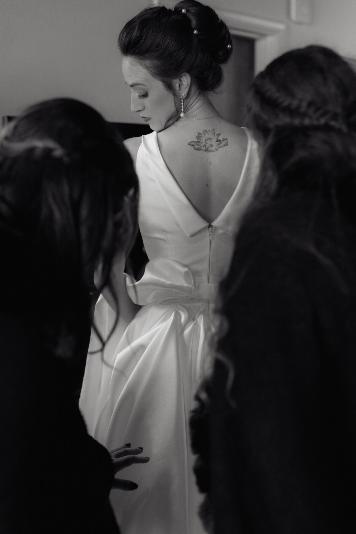Cinematic black-and-white documentary photo capturing an elegant bride as her bridesmaids help her prepare. Captured by luxury wedding photographers specializing in timeless and authentic wedding storytelling.