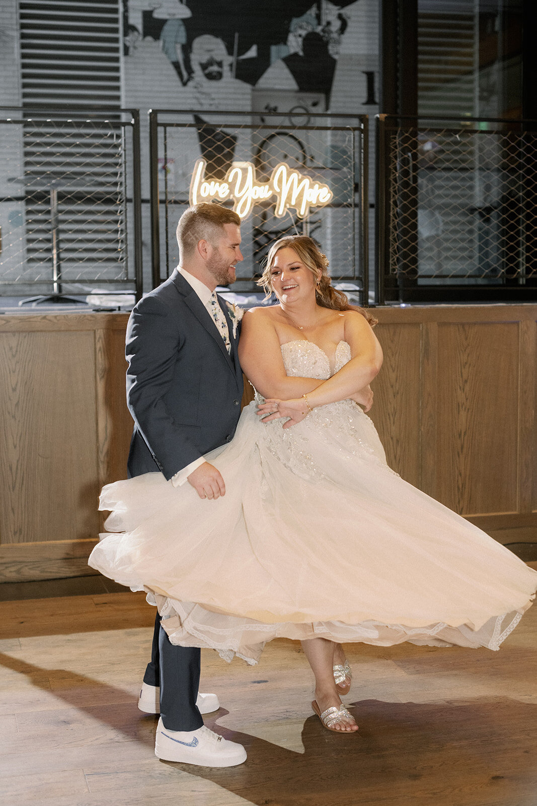 Bride and groom dance in front of an I love you more neon light on their wedding day.