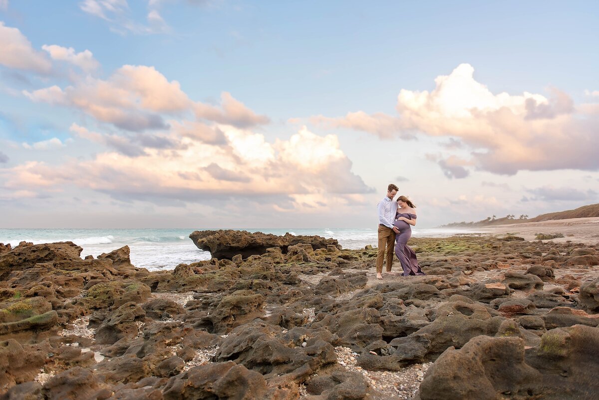 purple maternity dress on the beach with rocks and pretty sunset sky