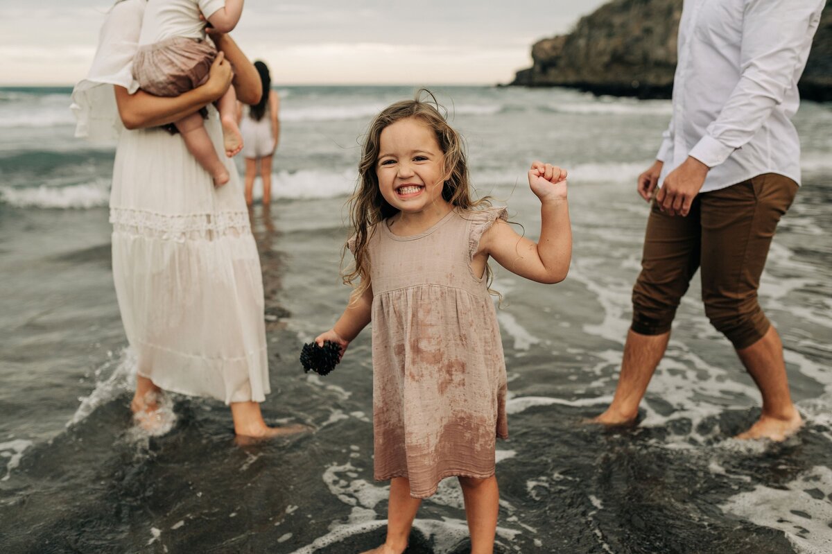 girl beach family photographer christchurch taylors mistake pink dress wet sandy water sister smile