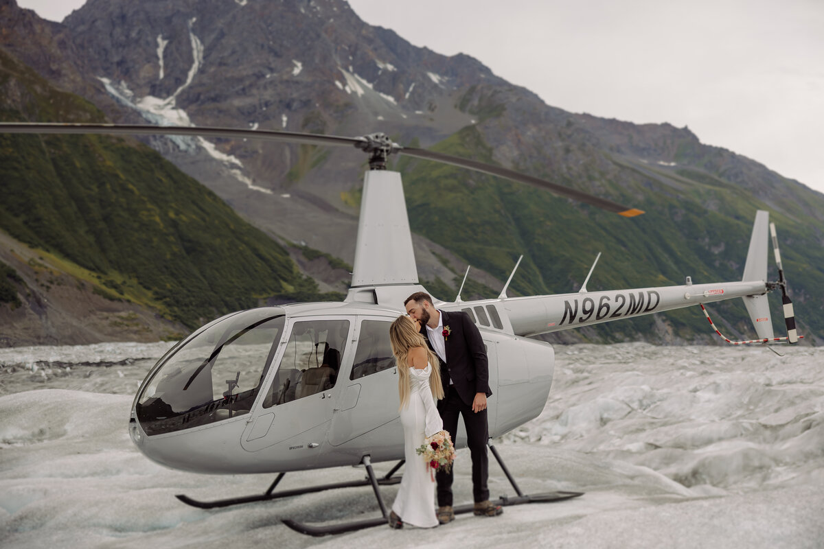 Couple posing in front of a helicopter on a glacier in Alaska during their elopement