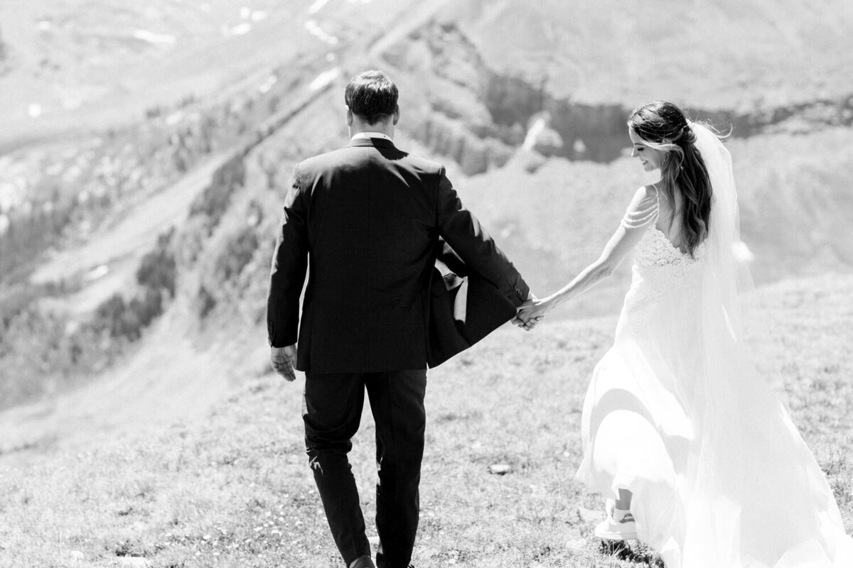 black-and-white-photograph-of-a-bride-and-groom-walking-hand-in-hand-during-their-mountain-wedding