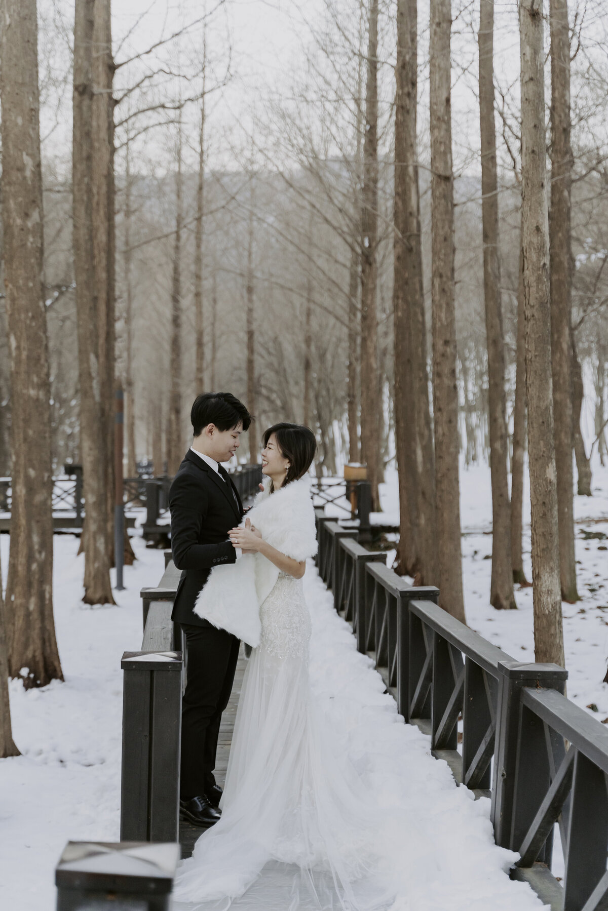 the bride wears a long white gown with white scarf while the groom wears black suit and tie