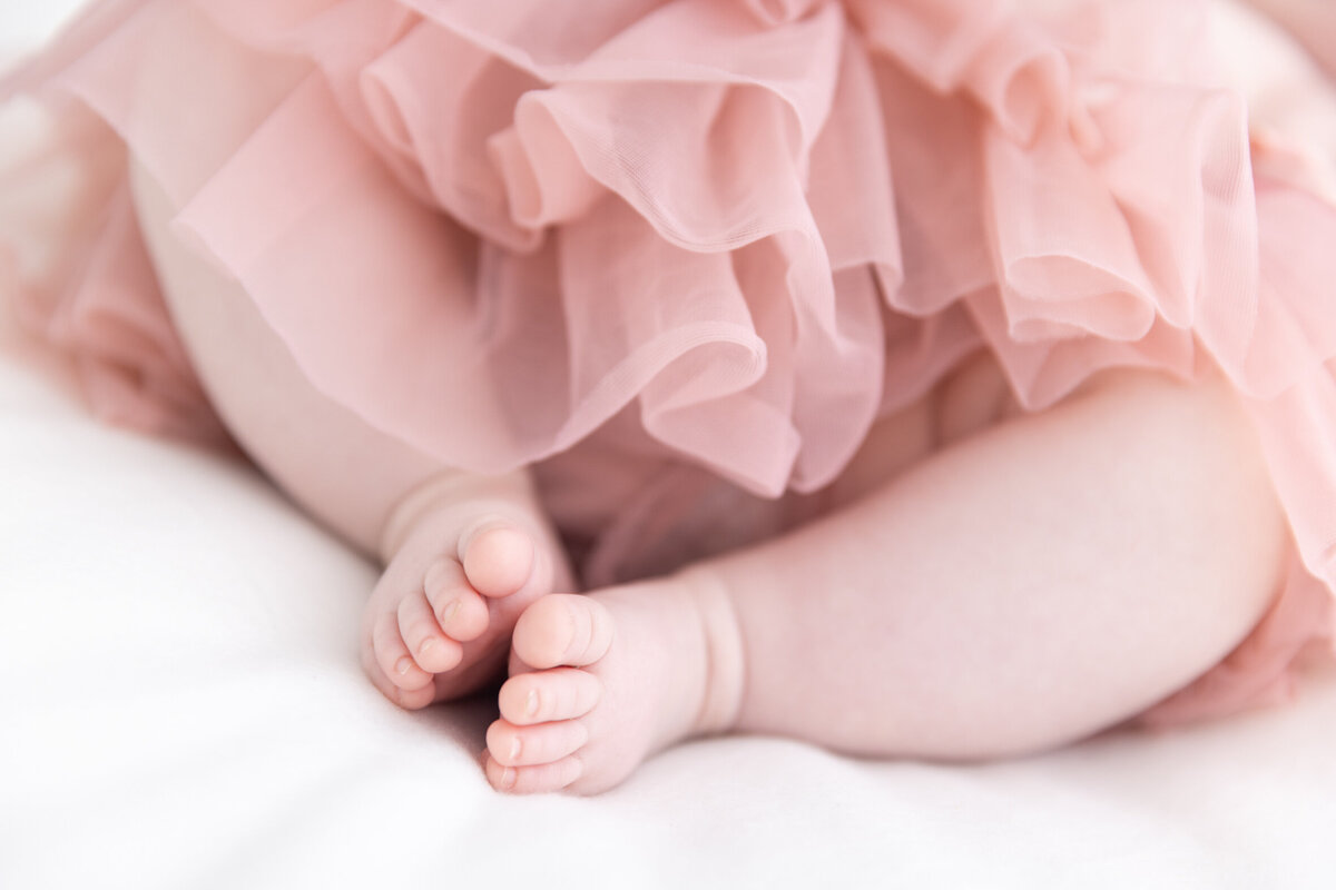 Detaljbilde av en babys føtter, man ser rosa tyllskjørt. Hvitt teppe. Fotografert i Studio Landmark, Fyllingsdalen. Fotografert i Studio Landmark, Fyllingsdalen.
