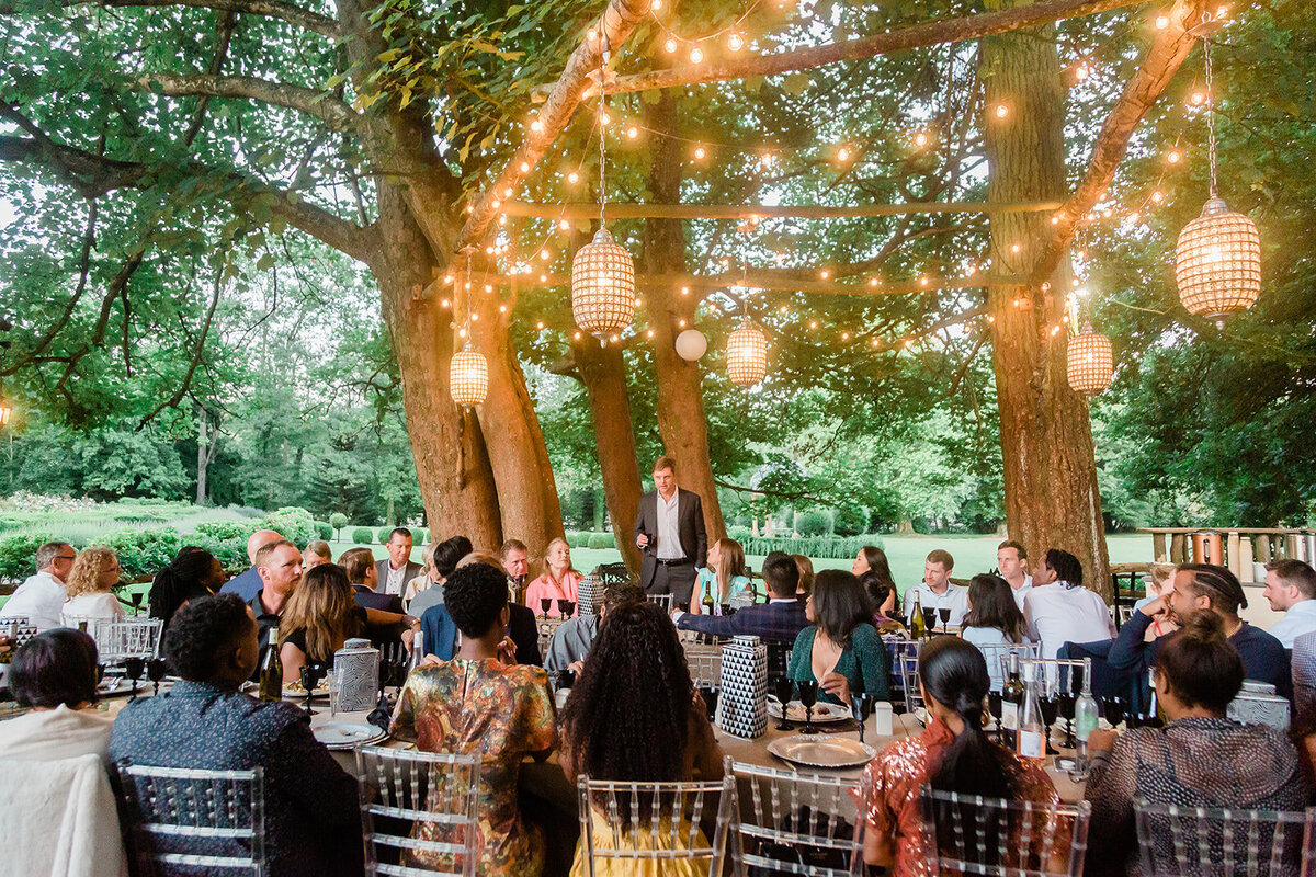 Bride or groom giving a speech during the pre-wedding welcome party in the gardens of Château Challain, captured in elegant, natural wedding photography.
