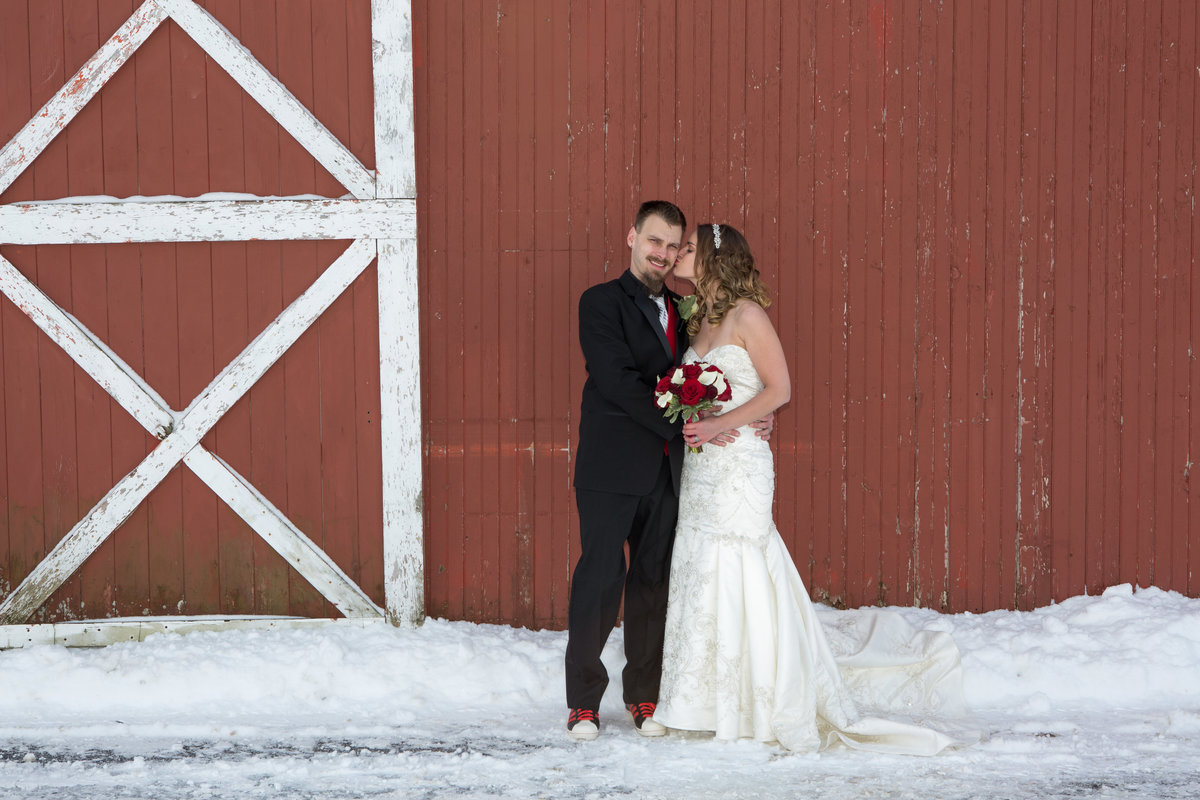 bride and groom in front of a barn in the winter