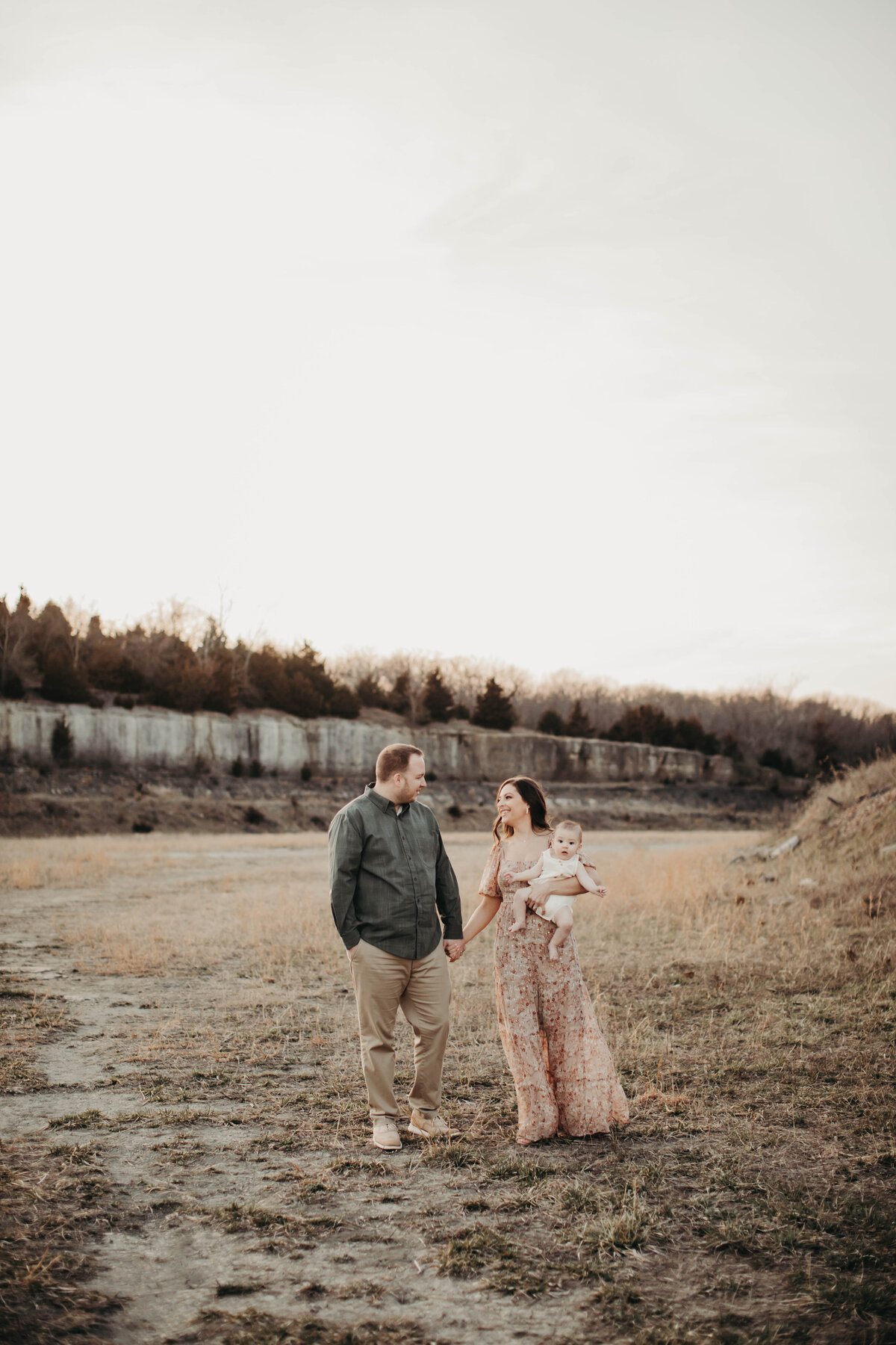 Mom and dad walking in open field while mom holds baby.