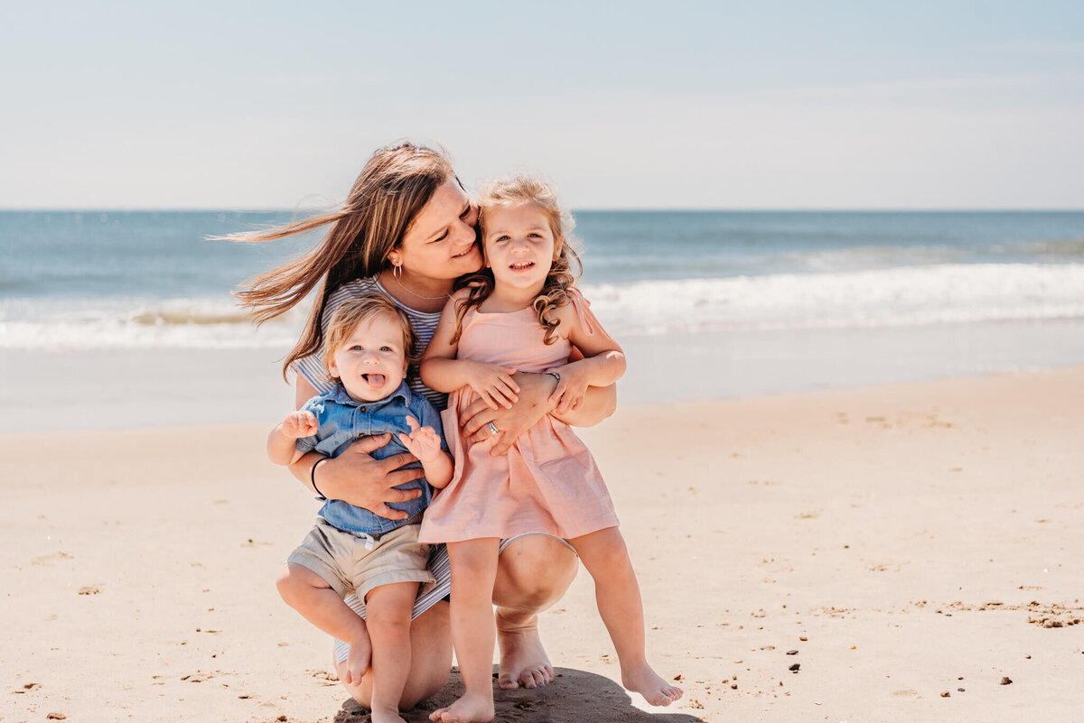 Mom kneeling on the beach holding her two young children during their Bethany Beach Family Photography session.