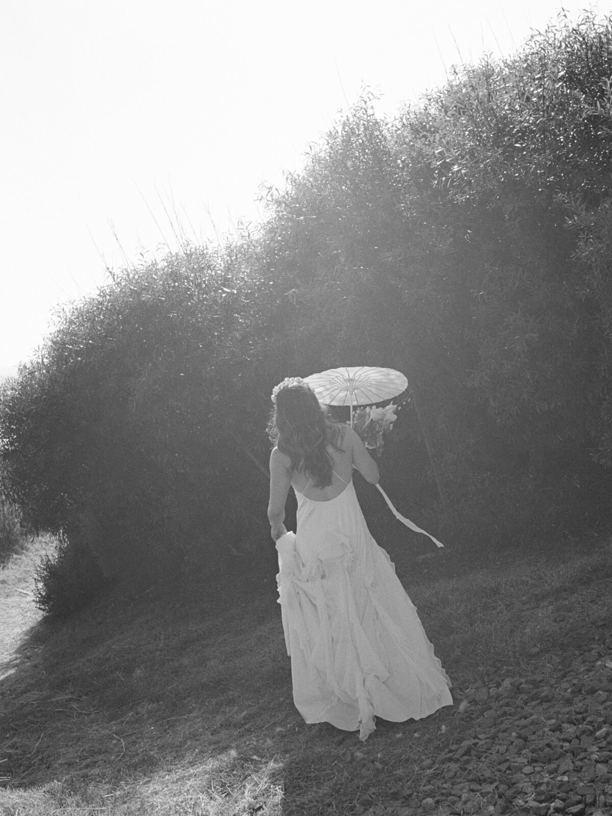 Solo bride elegantly holding a parasol as the sun sets, creating a romantic glow against the La Jolla landscape.