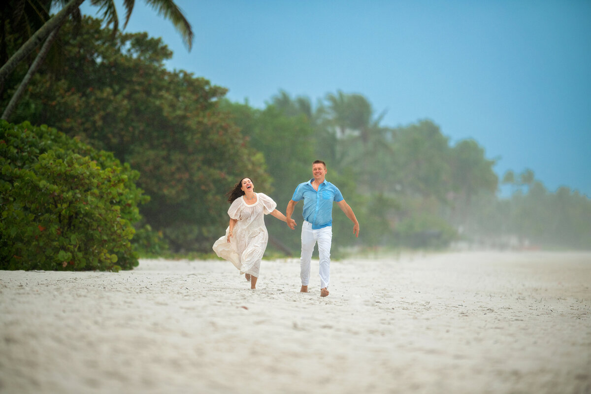 Couple having fun running in white Naples beach sand while holding hands