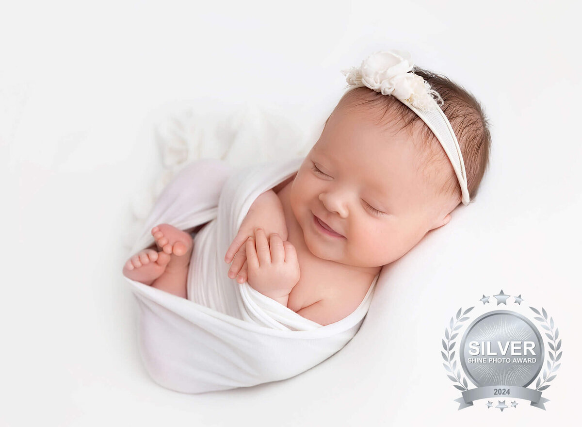 Newborn baby girl wrapped in white laying on a white blanket modern newborn pictures in Brooklyn NYC