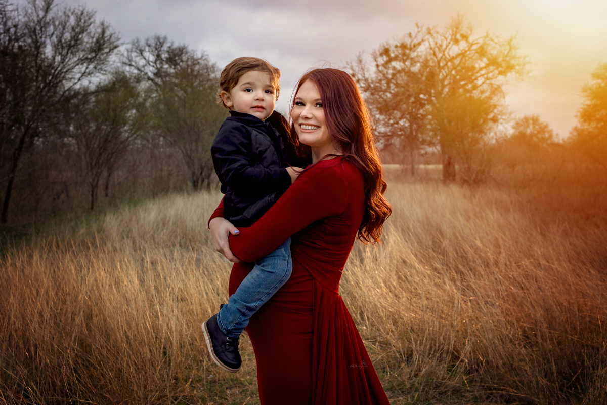 Radiate in winter with our styled maternity session near San Antonio. Laid-back parents, embrace the beauty of the season as our mom-to-be graces the winter field in a scarlet flying dress.
