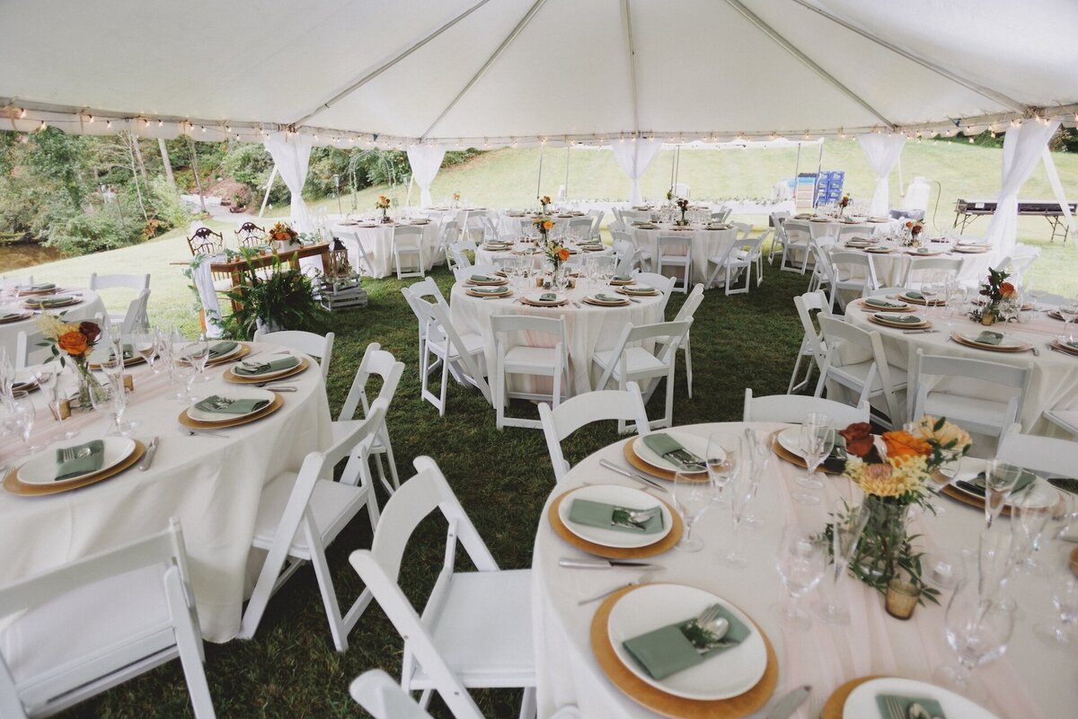 white tables with plates and chairs under a tent