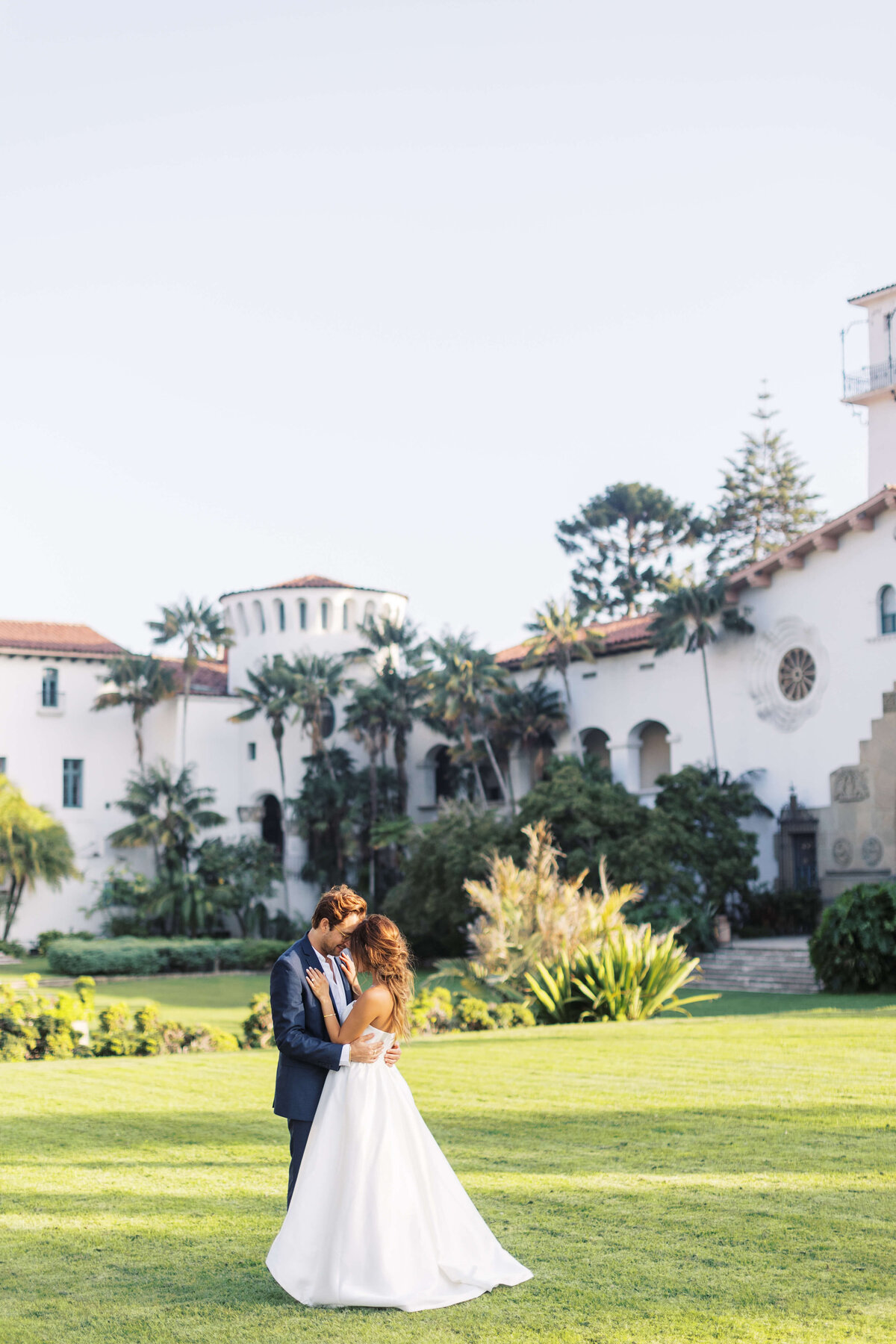 Husband and wife embrace each other in the field in front of Santa Barbara courthouse.
