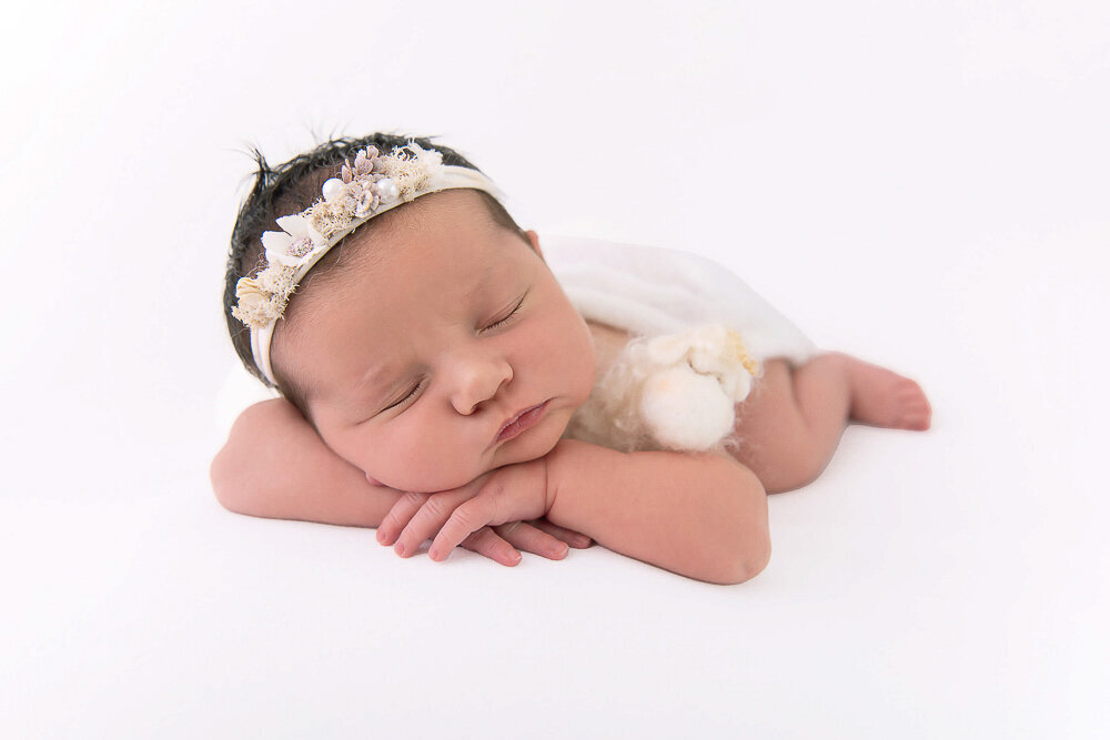 Newborn baby girl wearing a white headband holding a little lamb.