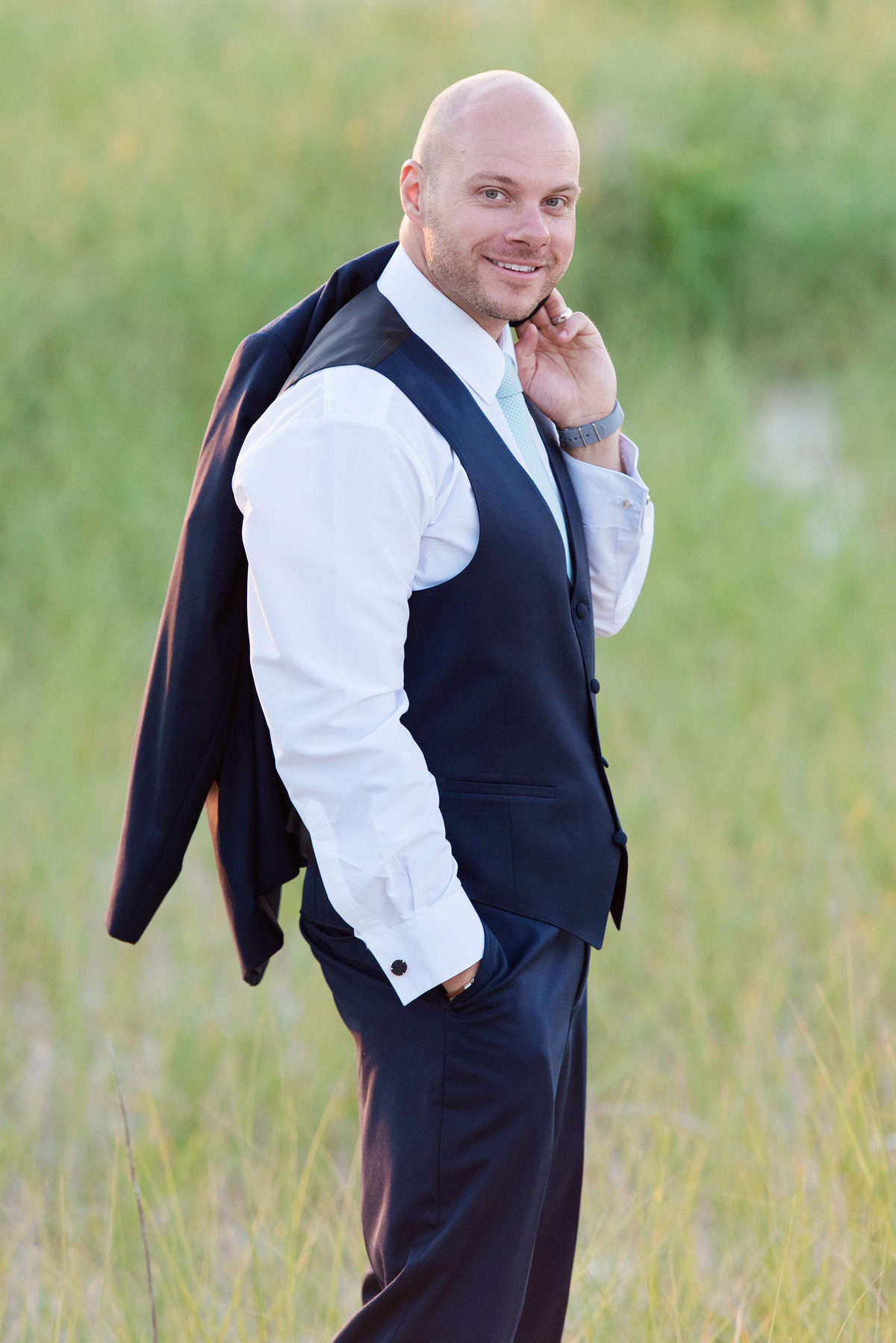photo of groom holding his tuxedo jacket over his shoulder on the beach from wedding reception at Pavilion at Sunken Meadow