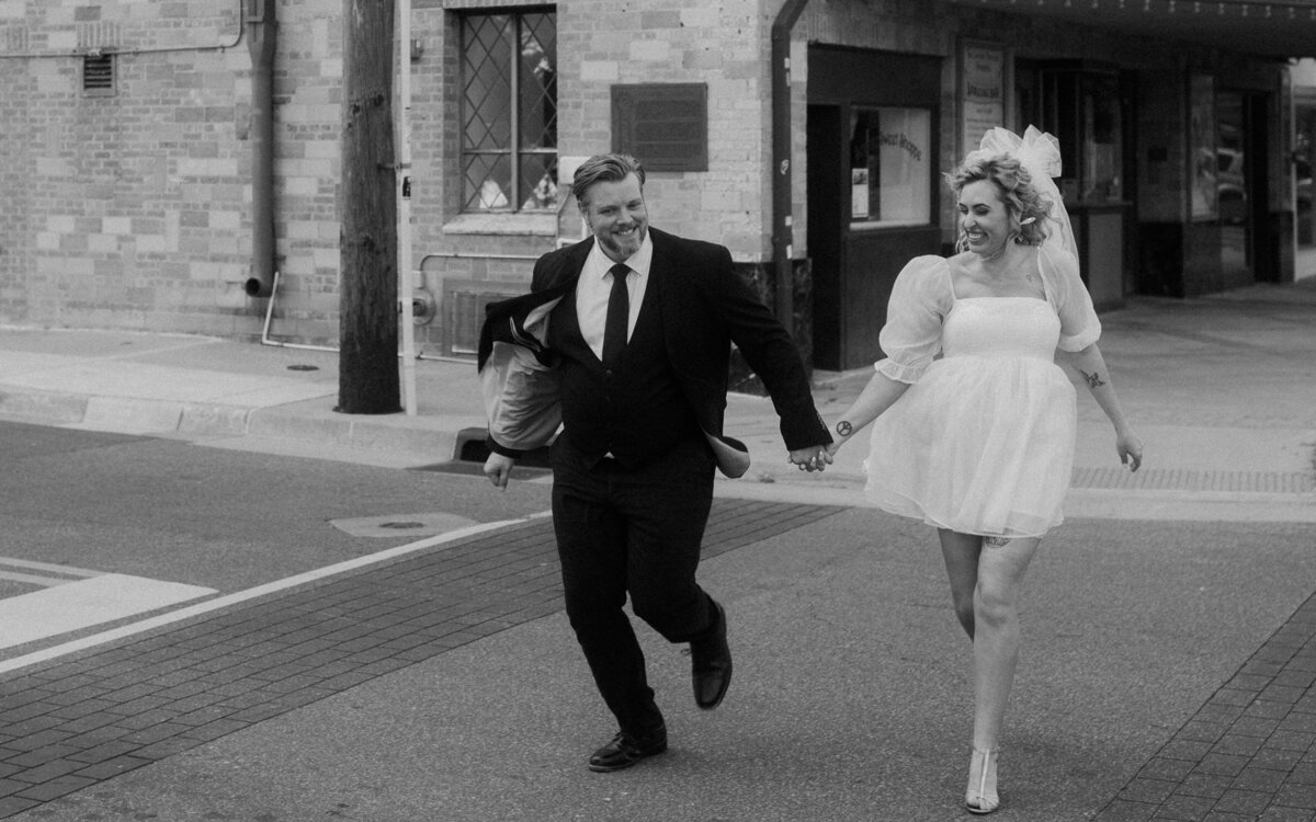 A joyful black and white scene of a couple running hand in hand across a street
