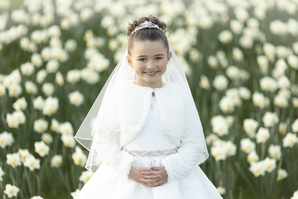 A young girl in a white dress stands in a field of white flowers for a New Jersey Communion Portrait Photographer