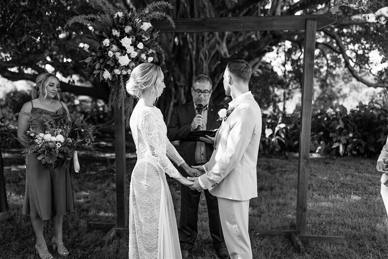 Experience the purest moments of love as Maddi and Jeremy embark on their journey together, captured in a timeless photograph of them holding hands, gazes locked on the celebrant.