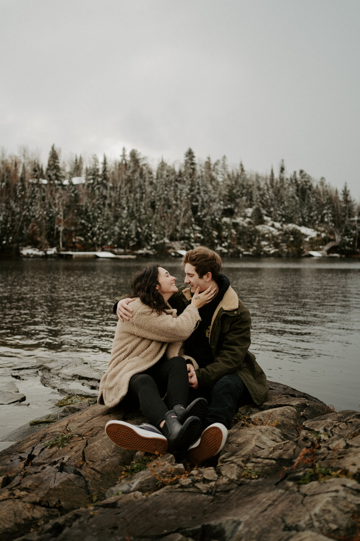 couple embracing on rock by lake