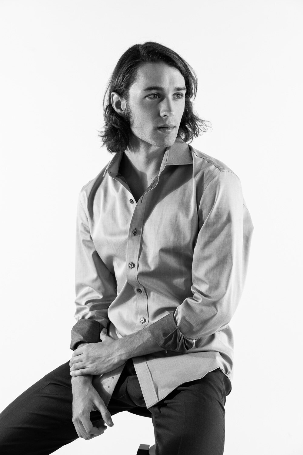Cinematic editorial portrait of a man seated on a stool in front of a white studio background