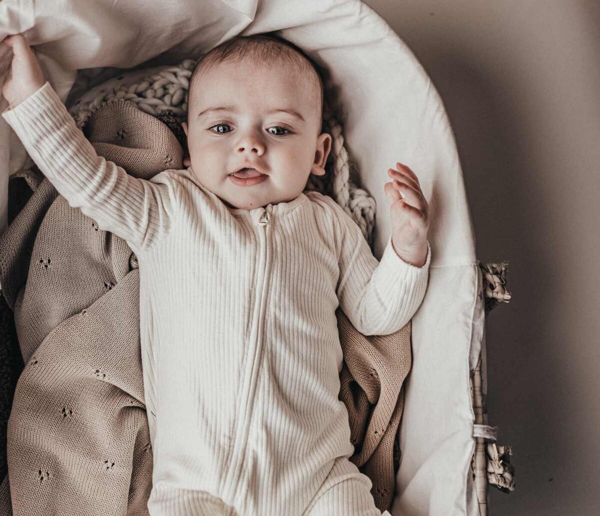 Ruua Hamdan Photography (Altrincham/Manchester, UK): A baby lies awake in a blanket-lined bassinet.