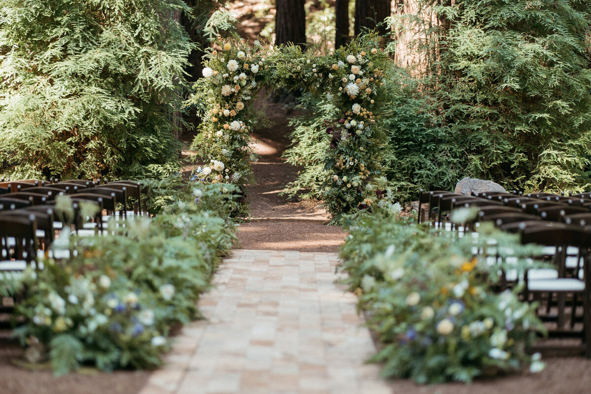 Fern and floral aisle arrangements leading to lush ceremony arch