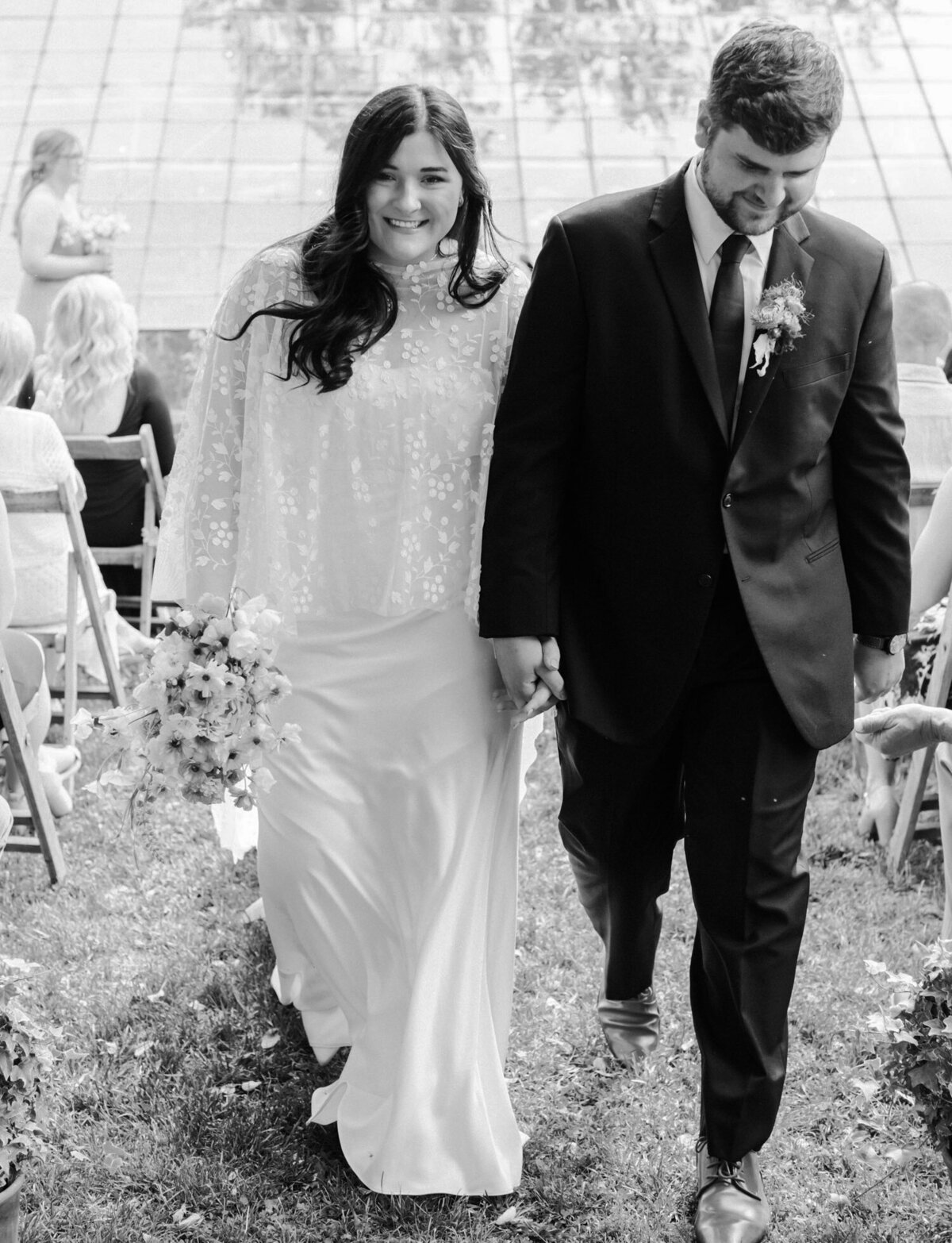 smiling couple walks down aisle, recessional at Glass House Community