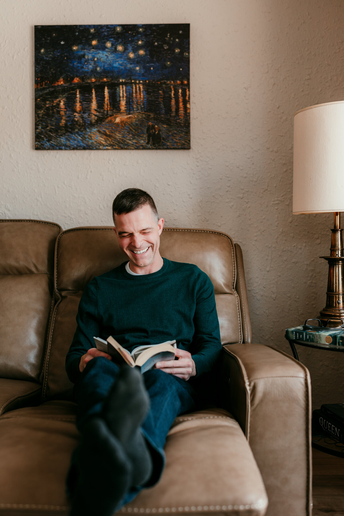 Man sitting on a couch reading a book, highlighting his personality in a professional dating profile photo session.