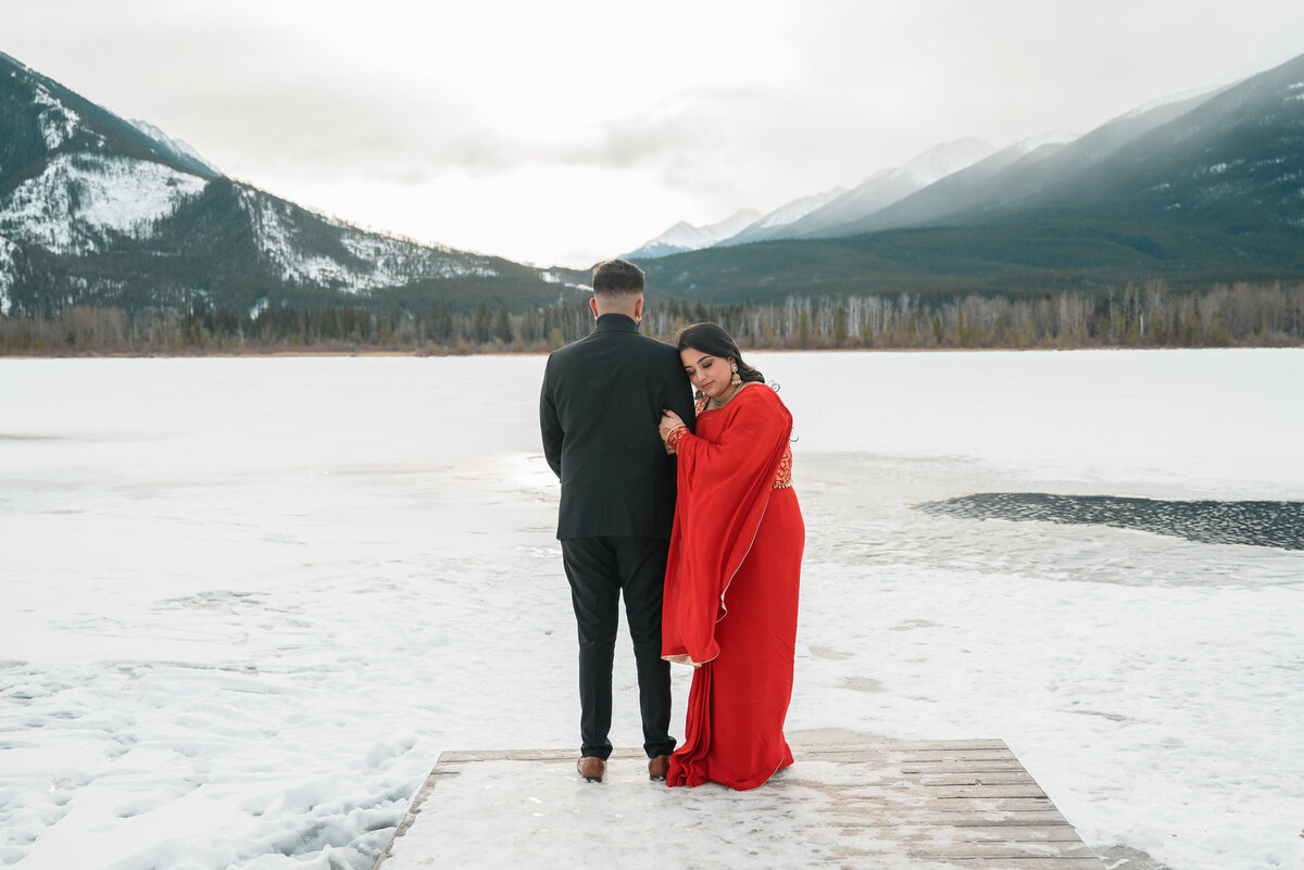 Engaged couple standing in snow, bride-to-be wearing a red sari at Vermilion Lakes.