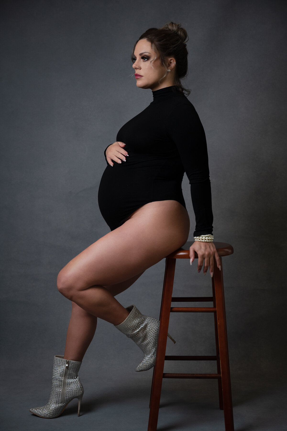 A woman showing her pregnant belly sitting on a stool