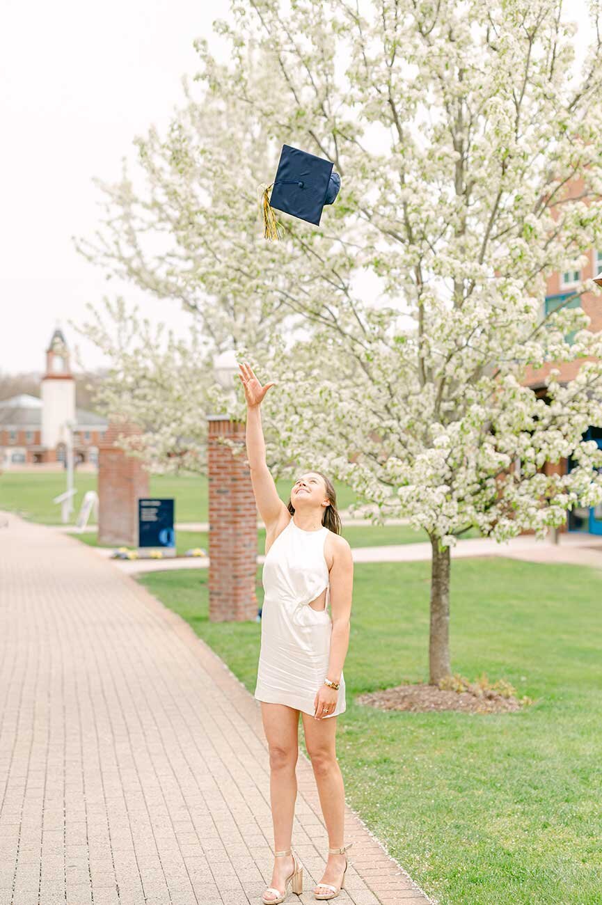 girl in white dress throwing graduation cap