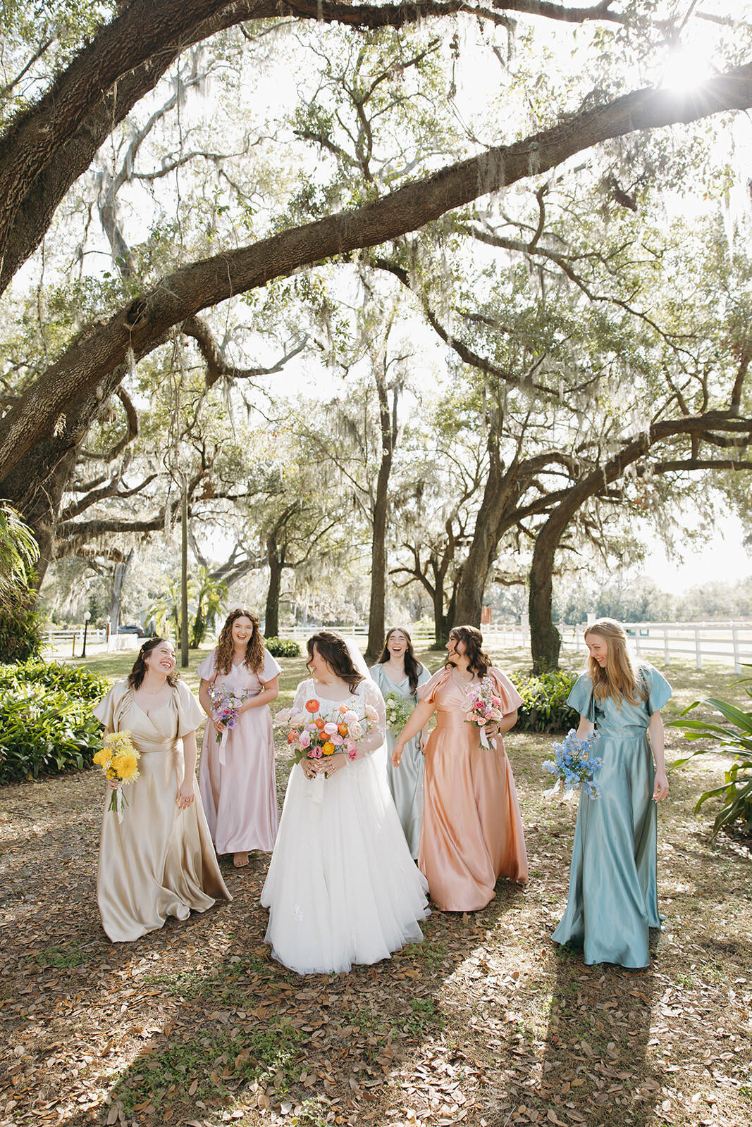 Bridesmaids walking under the oak trees at Uliana Estate in Lakeland Florida, wearing soft pastel gowns.