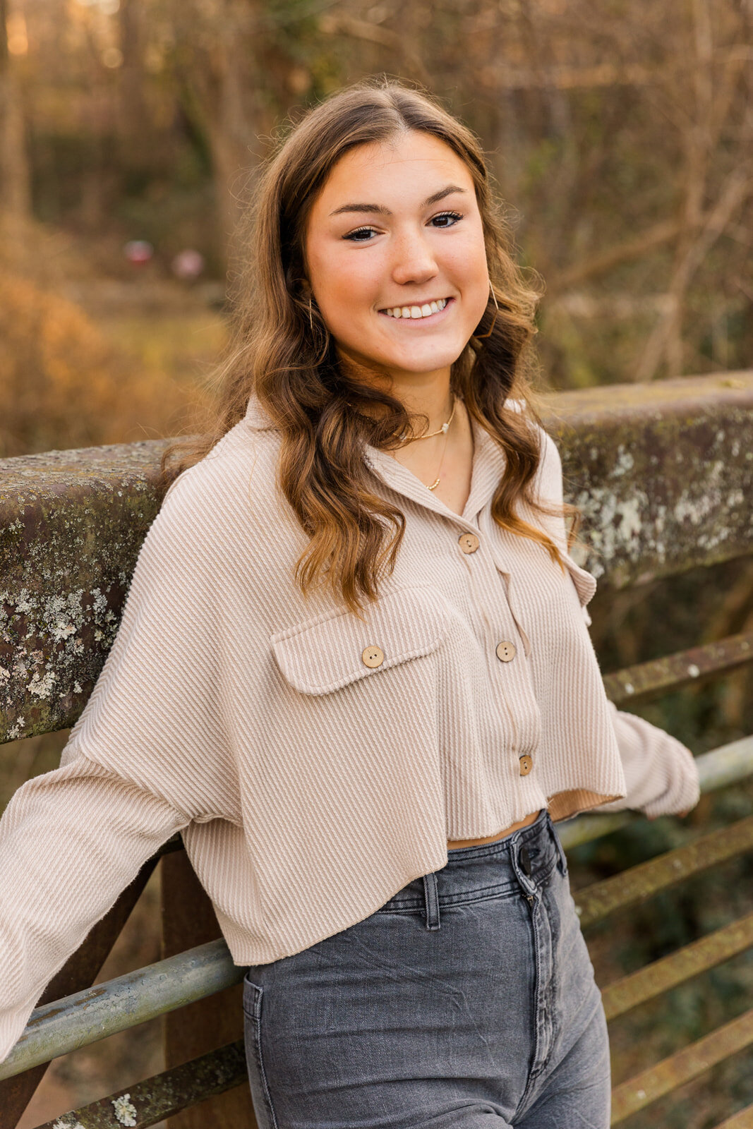 Senior girl standing on a park bridge wearing black jeans and beige top during Atlanta park photo session with Laure Photography