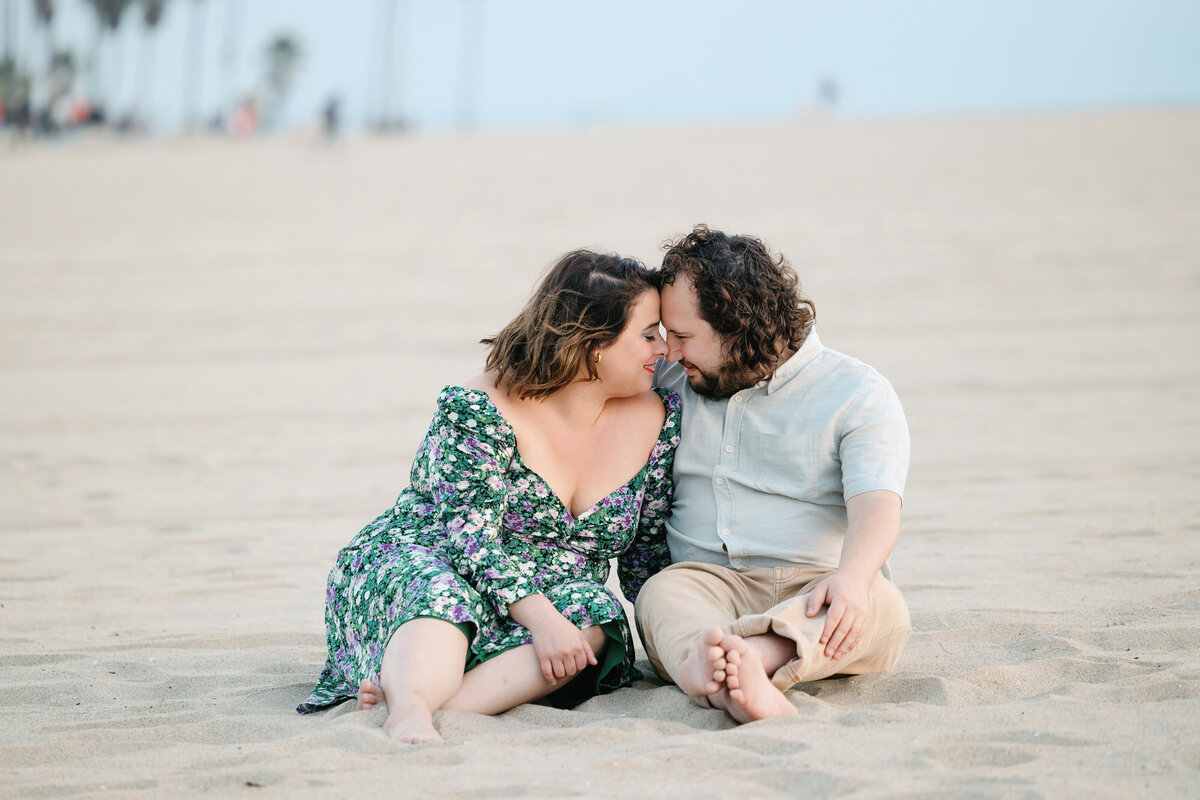 A couple sitting in the sand with their foreheads together