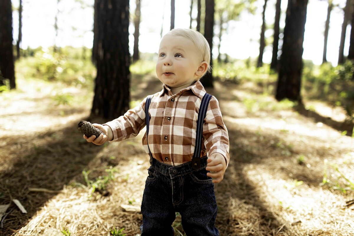 Birthday boy in suspenders and overalls, surrounded by pine trees, looking joyful and carefree