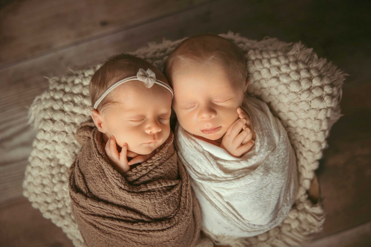 Twin newborn babies wrapped in textured wraps sleeping side by side