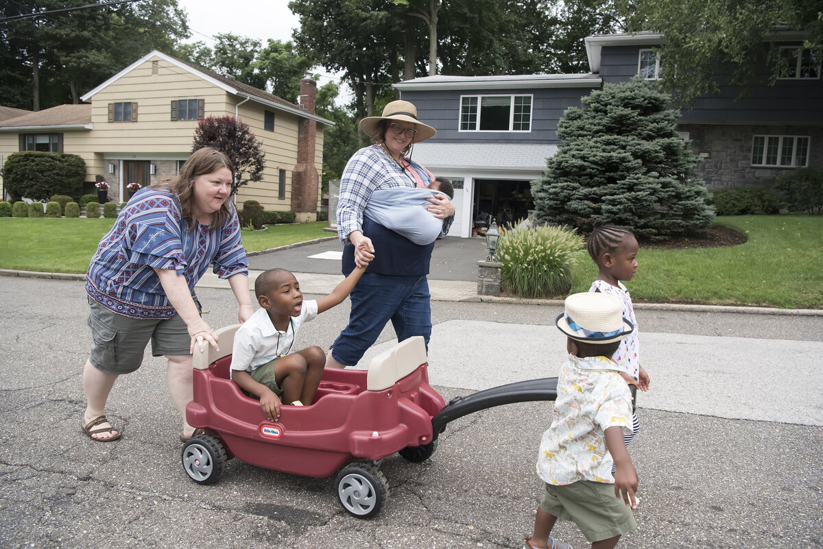 A family of six walking in the street as on of the kids pulls a wagon with another one sitting in it