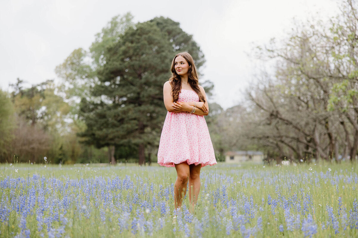 senior girl in short pink dress laying in a field of bluebonnets