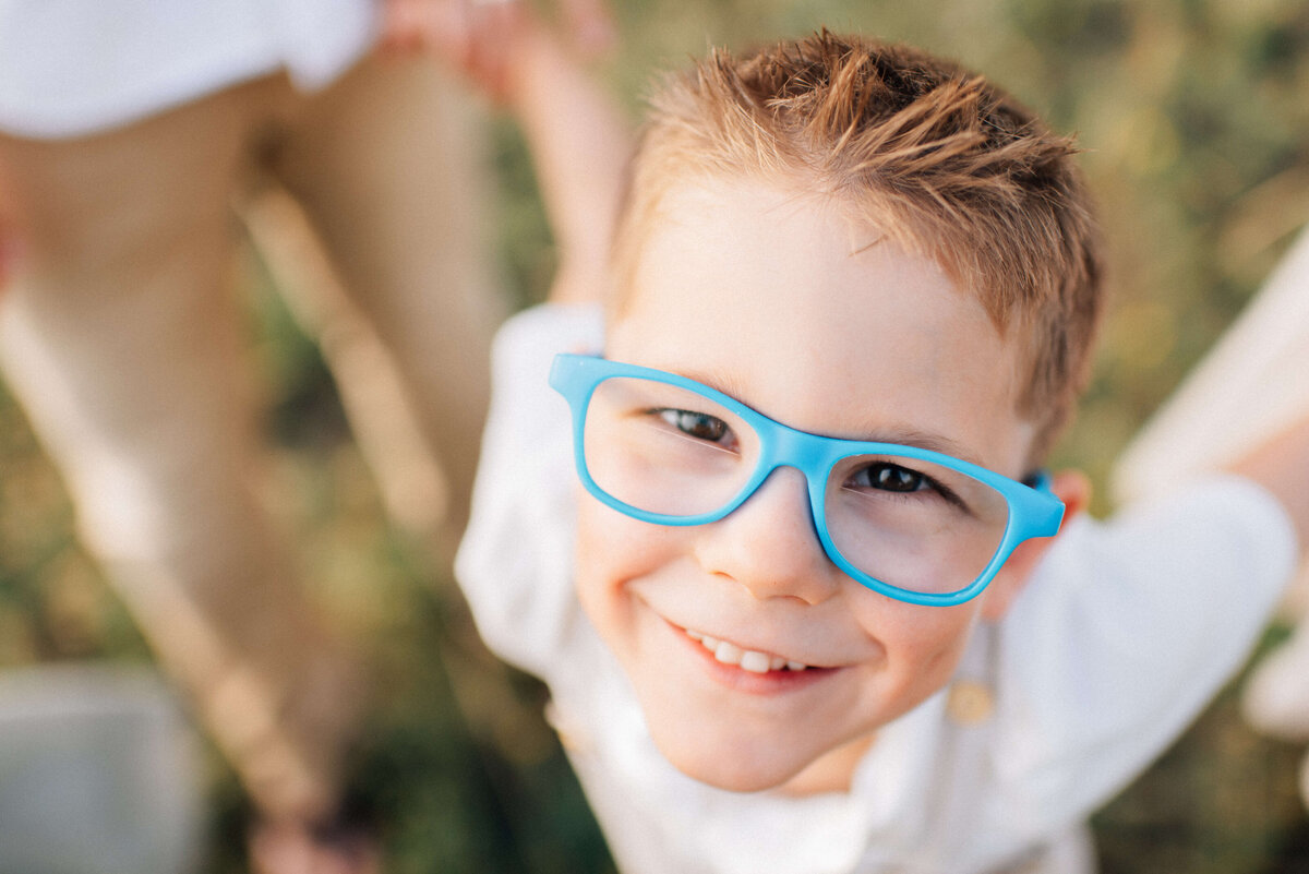 boy with blue glasses smiling and looking up at the photographer
